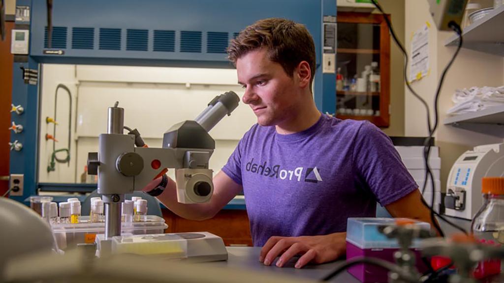 生物学 student with microscope in ProRehab t-shirt